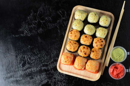 A set of various rolls with chopsticks in a wooden bamboo plate on a black wooden background with ginger and wasabi. Selective focus.の写真素材