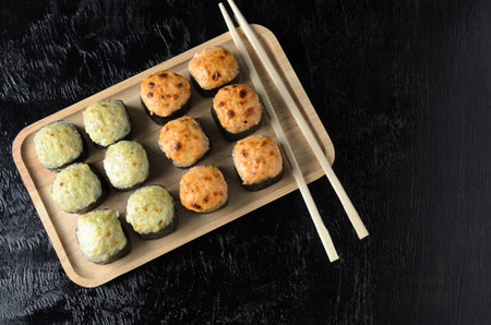 A set of seafood rice rolls wrapped with thin leaves of dried sea grass in a wooden platter on a black wooden background. Selective focus.の写真素材