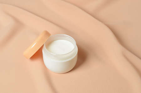A jar of cream for caring for delicate skin on a wavy beige background made of chiffon. Selective focus.の写真素材