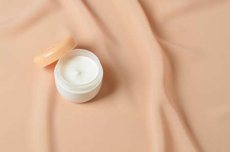 A jar of cream for caring for delicate skin on a wavy beige background made of chiffon. Selective...