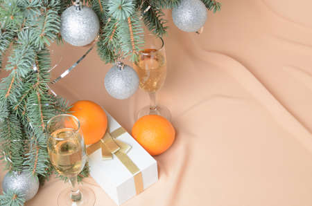 Christmas tree decorated with silver balls, a gift box, sparkling wine glasses on a background with flesh-colored waves. Selective focus.の写真素材