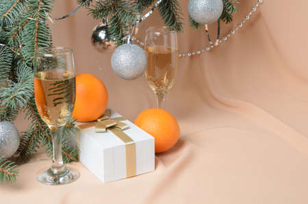 Christmas. A New Year's composition made of branches of a Christmas tree decorated with silver balls, a gift box, sparkling wine glasses on a background with flesh-colored waves. Selective focus.の写真素材