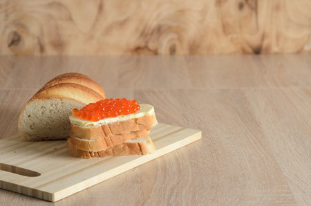 Sandwich with butter and red caviar on a cutting board with slices of white bread. Selective focus.