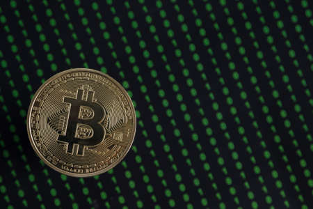 Golden Bitcoin, binary code on a blurry black background. Selective focus.