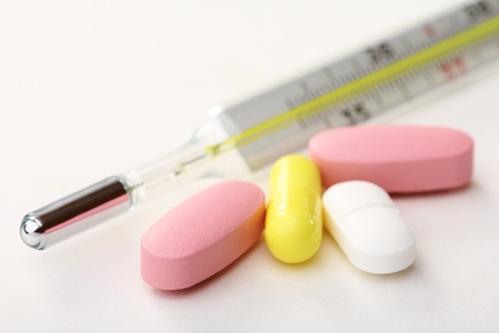 Medical thermometer and pills on a white background.