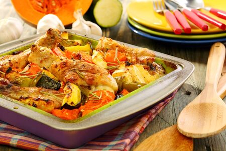 Baked chicken with vegetables and spices on a wooden table の写真素材