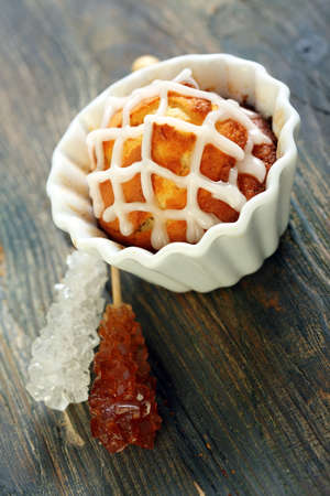 Cupcake with icing, stick with white and brown sugar on a wooden table.