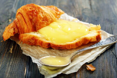 Croissant with cream and teaspoon on a wooden table.の写真素材