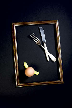 Egg in a stand, fork and knife in frame on a black background.の写真素材