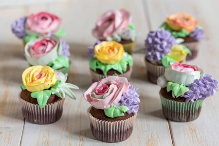 Cupcakes with cream-colored flowers on a white wooden table.の写真素材