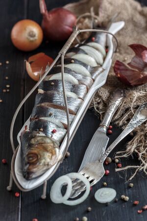 Herring with onions and spices in a serving dish on a wooden table.の写真素材