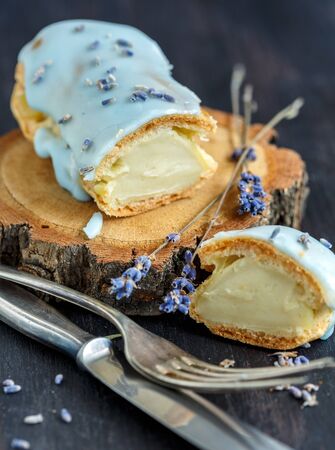 Eclair and lavender flowers on the wooden stand close up.