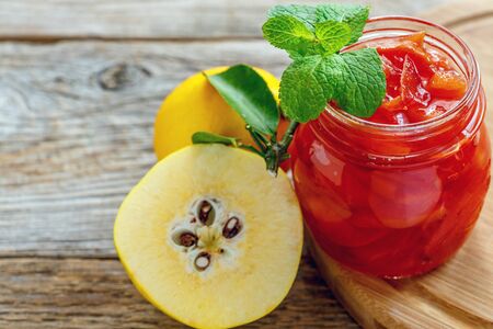 Quince jam in glass jar and sprig of mint on a wooden table.の写真素材