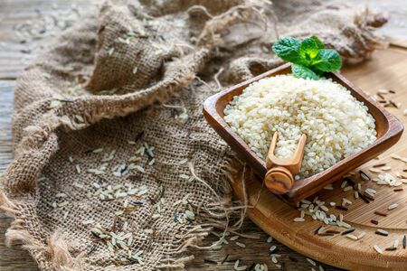 White rice in wooden bowl and a rustic burlap on the table.の写真素材
