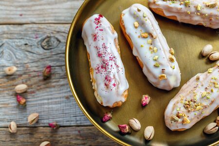 Vanilla eclairs with small roses and pistachio on old wooden table.