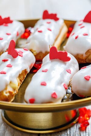 Eclairs with the decor of red hearts on a bronze stand close up, selective focus.