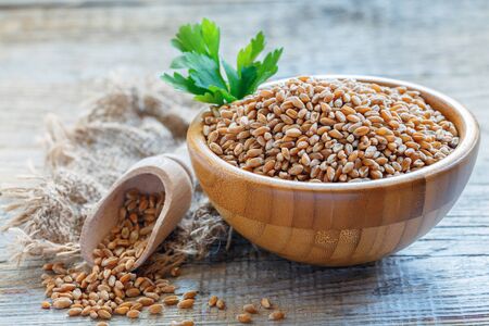 Whole grain wheat in a wooden bowl on a table with old sackcloth.の写真素材