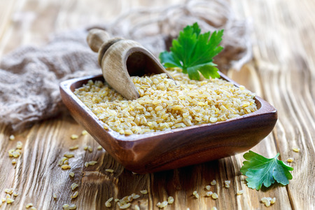 Organic bulgur and scoop in a bowl on a wooden table.の写真素材