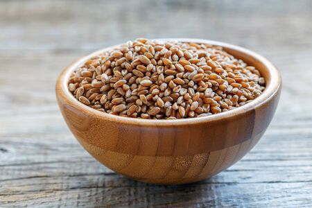 Wheat in a round bowl on old wooden table.