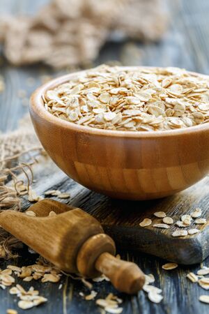 Wooden bowl with oat flakes and the scoop on an old table, selective focus.の写真素材