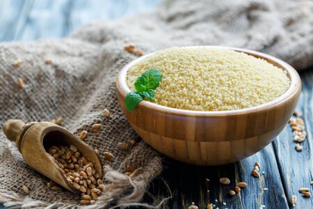 Couscous in a wooden bowl and scoop with wheat on old rustic table, selective focus.の写真素材