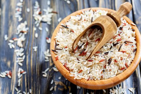 Scoop into a bowl with mixture of four types of rice close-up on dark wooden background.の写真素材