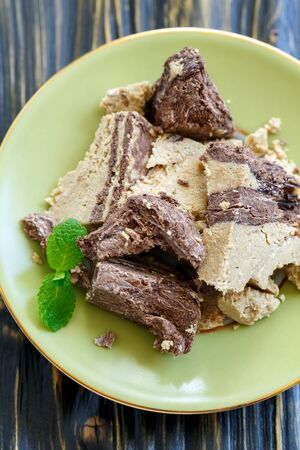 Plate with tahini halva with chocolate and mint close up on wooden background.