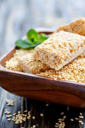 Wooden bowl with sesame and honey bars on the old table, selective focus.