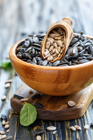 Sunflower seeds and wooden scoop in bowl on old kitchen table, selective focus.の写真素材