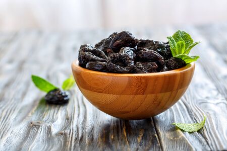 Prunes and mint in a bowl on old wooden table, selective focus.の写真素材