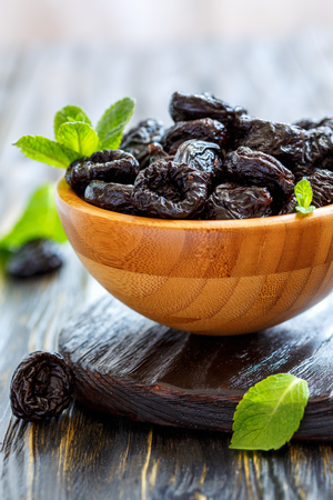 Bowl of dried black plums on wooden stand, selective focus.の写真素材