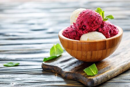 Balls of lemon ice cream and berries in bowl on wooden table, selective focus.