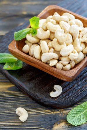 Cashews and mint leaves in a bowl on old wooden table, selective focus.の写真素材