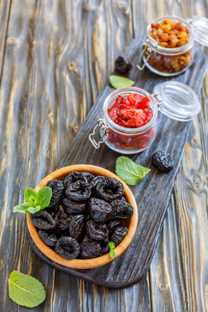 Wooden bowl with prunes and a jar with dried fruits on a serving board.の写真素材