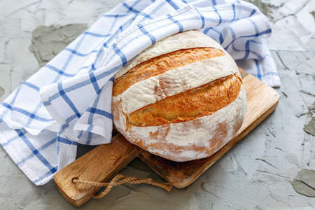 Fresh homemade bread under the linen towel on a wooden board.