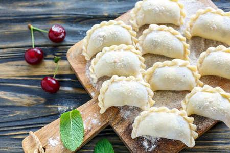Board with homemade dumplings with cherries on old wooden table, selective focus.の写真素材