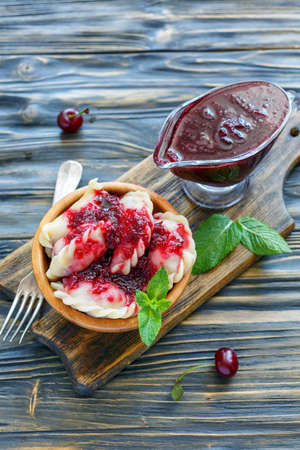 Bowl of the cherry dumplings and a gravy boat with berry sauce on a wooden table.の写真素材