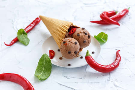 Chocolate ice cream with chilli in a waffle cone on a white plate.