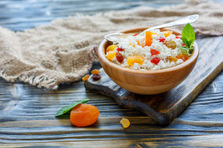 Homemade cottage cheese with dried fruit in a bowl on old wooden table, selective focus.の写真素材