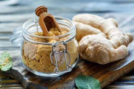 Ground ginger in jar and the ginger root on old wooden table, selective focus.