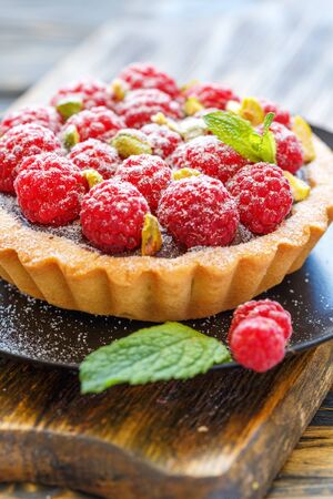 Tartlet with fresh raspberries, chocolate and pistachios on a wooden stand, selective focus.の写真素材