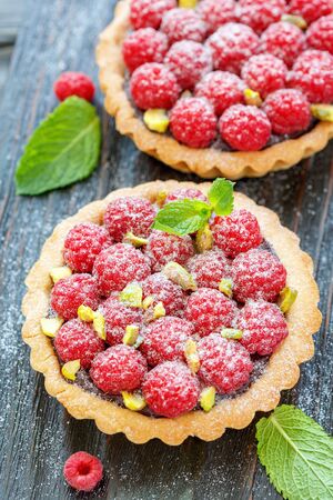 Wooden stand with the tartlets with fresh raspberries and pistachios, selective focus.の写真素材