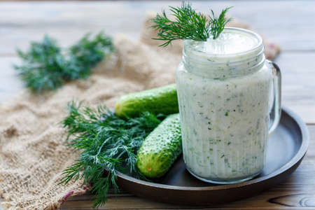 Useful smoothies of yogurt, cucumber and dill in a glass jar on wooden plate, selective focus.の写真素材