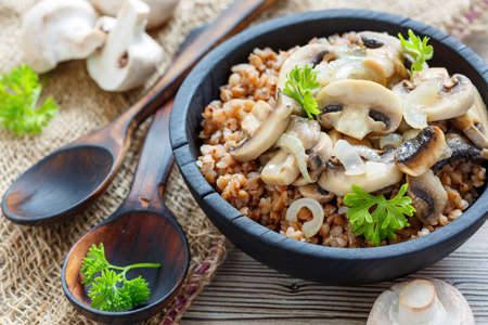 Boiled buckwheat with fried mushrooms and onions in a wooden bowl closeup, selective focusの写真素材