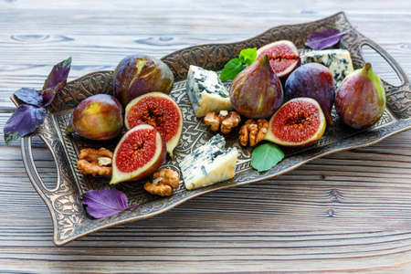 Tray with blue cheese, figs and purple basil on a wooden table.