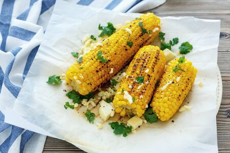 Sheet of parchment with corn on the cob grilled with cheese and cilantro.