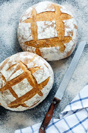Delicious homemade bread and bread knife on the dark table dusted with flour.
