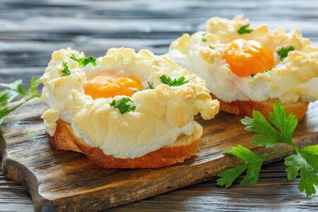 Bread with baked eggs Orsini and parsley leaves on a wooden stand, selective focus.の写真素材