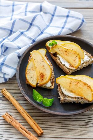 Crostini with ricotta, caramelized pear and cinnamon on a wooden dish.の写真素材