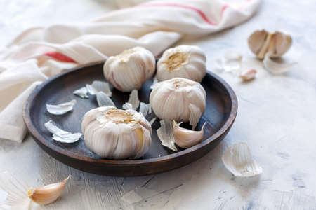 Garlic cloves in wooden dish on white table, selective focus.